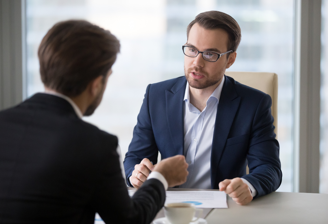 Two businessmen sat at a table using their improved negotiation skills. 