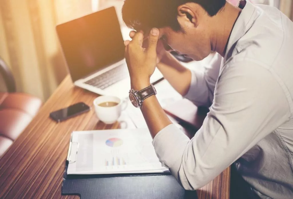 A team member in the workplace leaning over his desk in frustration due to his manager's though process affecting his performance and wellbeing.