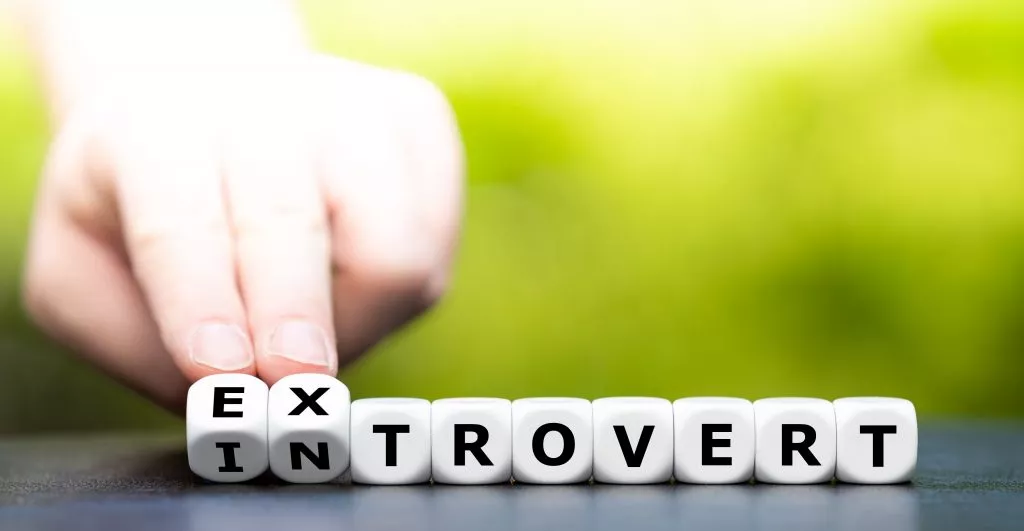 Hands turning dice to change word from introvert to extrovert, two types of people that need help working together at work 