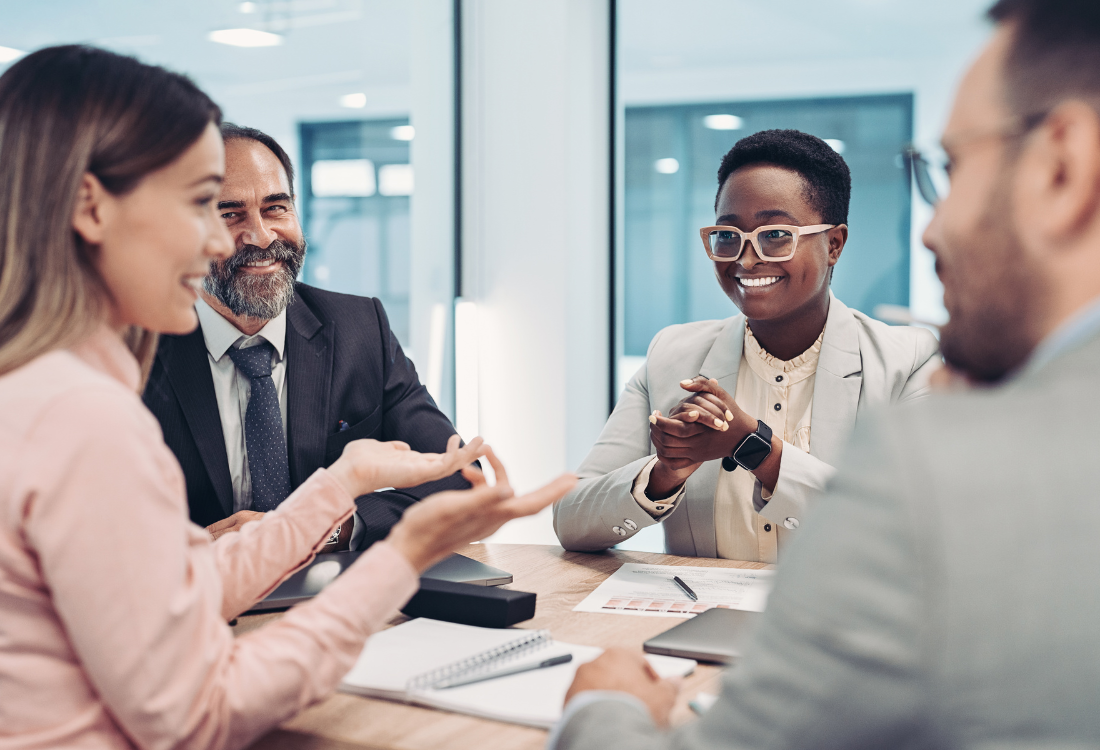 Happy employees who are sat around a table smiling because they have had professional development and leadership training to support the growth of the business they are working for.